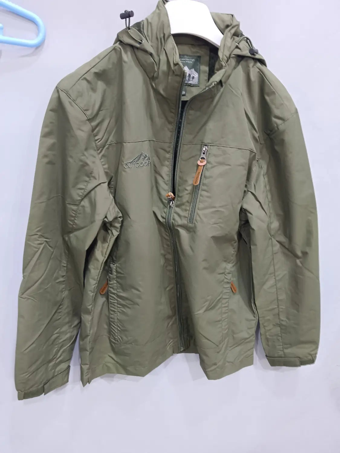 Chaqueta de senderismo con capucha impermeable color verde oliva, con bolsillos con cremallera y tiradores color cuero marrón, diseñada para actividades al aire libre.