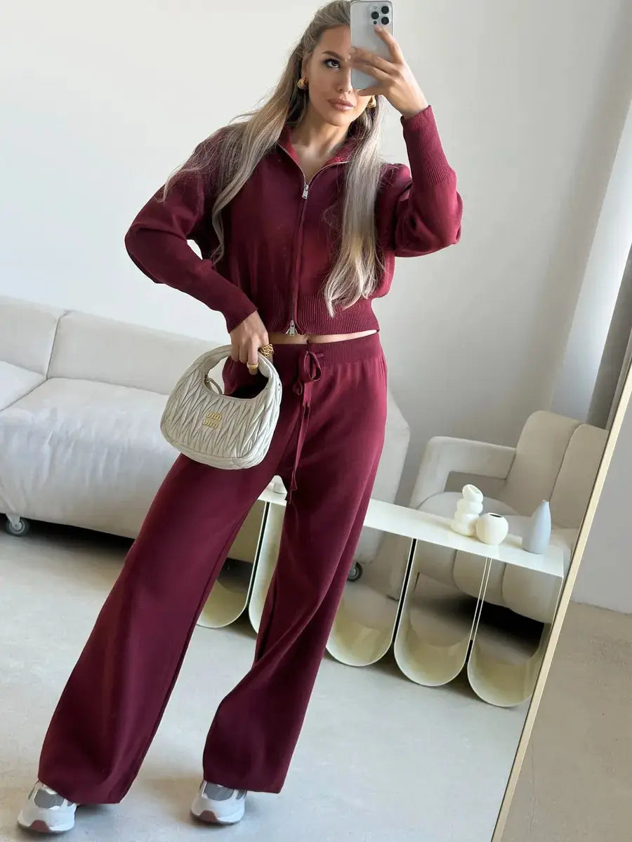 A cream-colored quilted handbag with a structured rounded shape and small gold-tone logo paired with a women’s knit zip up cardigan and wide leg pant set.