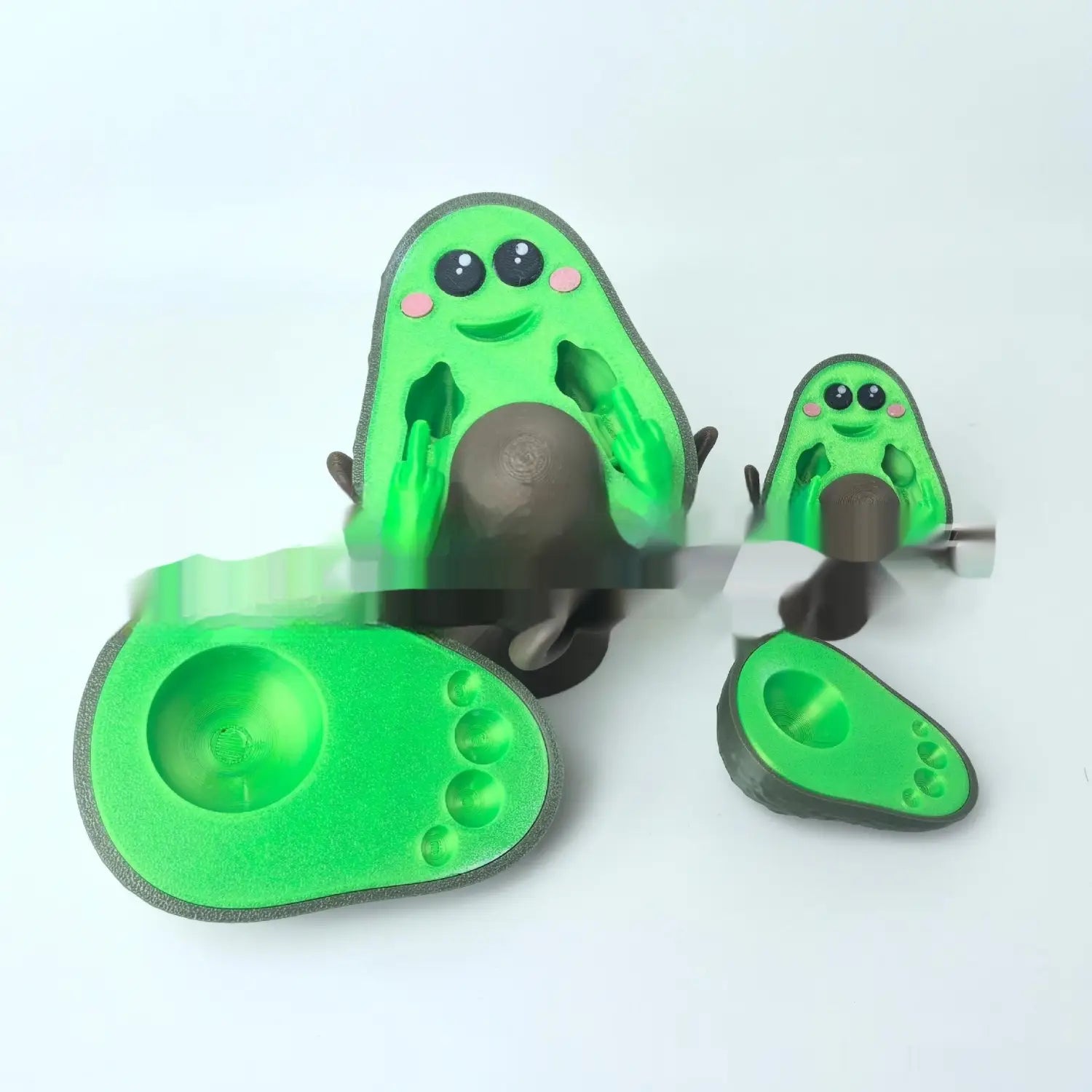 Green avocado-shaped silicone phone stand with cute cartoon face and textured grip designed as a 3d printed desk toy measuring 6.5cm.