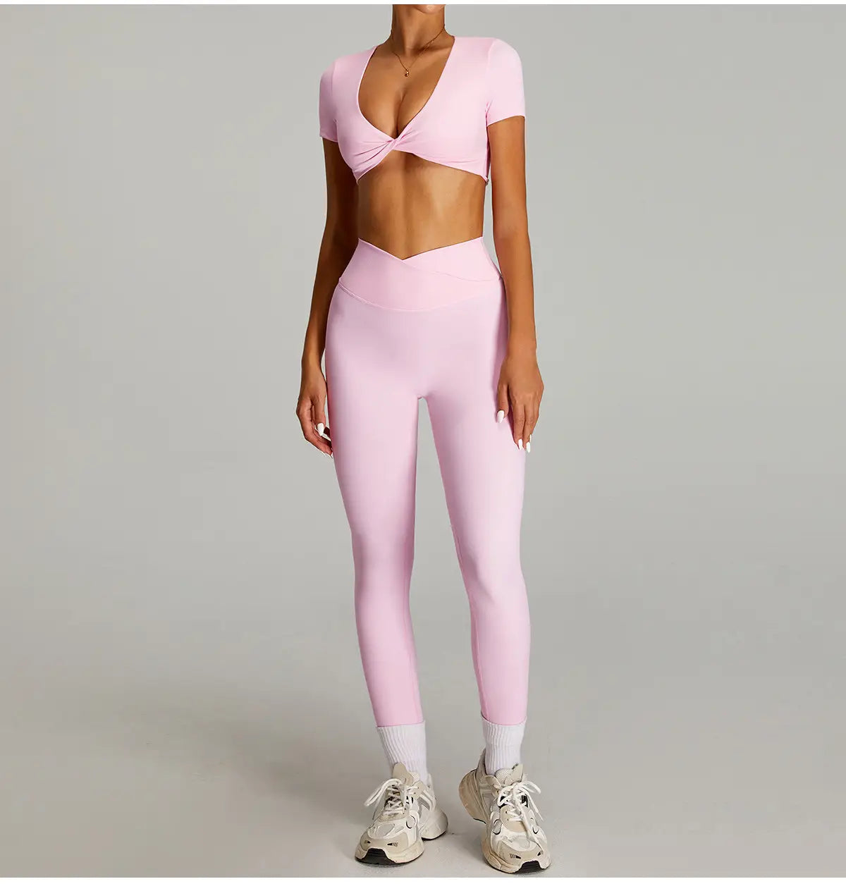 Ensemble de sport rose à deux pièces, avec un haut court torsadé à l’avant et des leggings de sport taille haute effet nu à séchage rapide, fabriqués dans un tissu lisse et extensible.