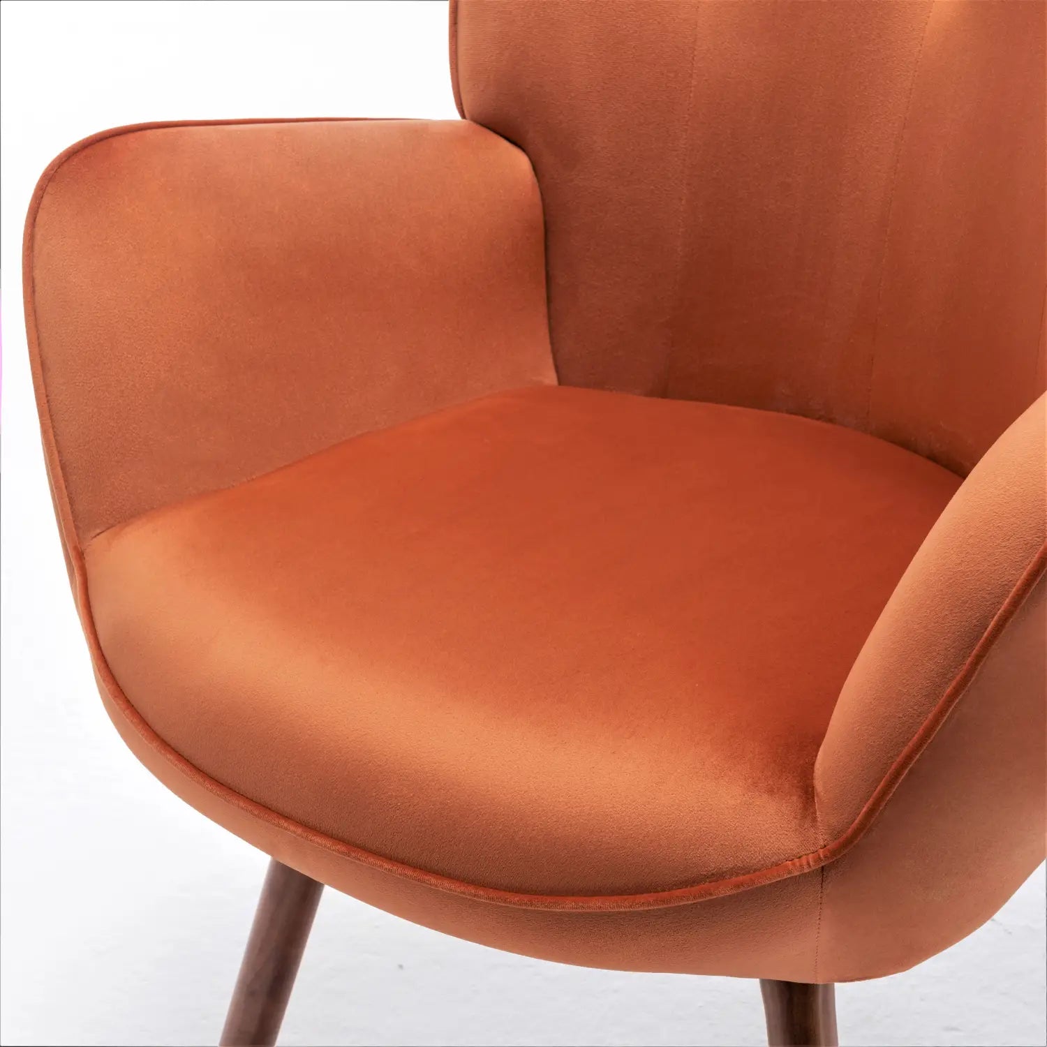 Una silla de acento tipo wingback de estilo moderno de mediados de siglo en terciopelo naranja quemado, con una textura suave y esponjosa y líneas suavemente curvas.