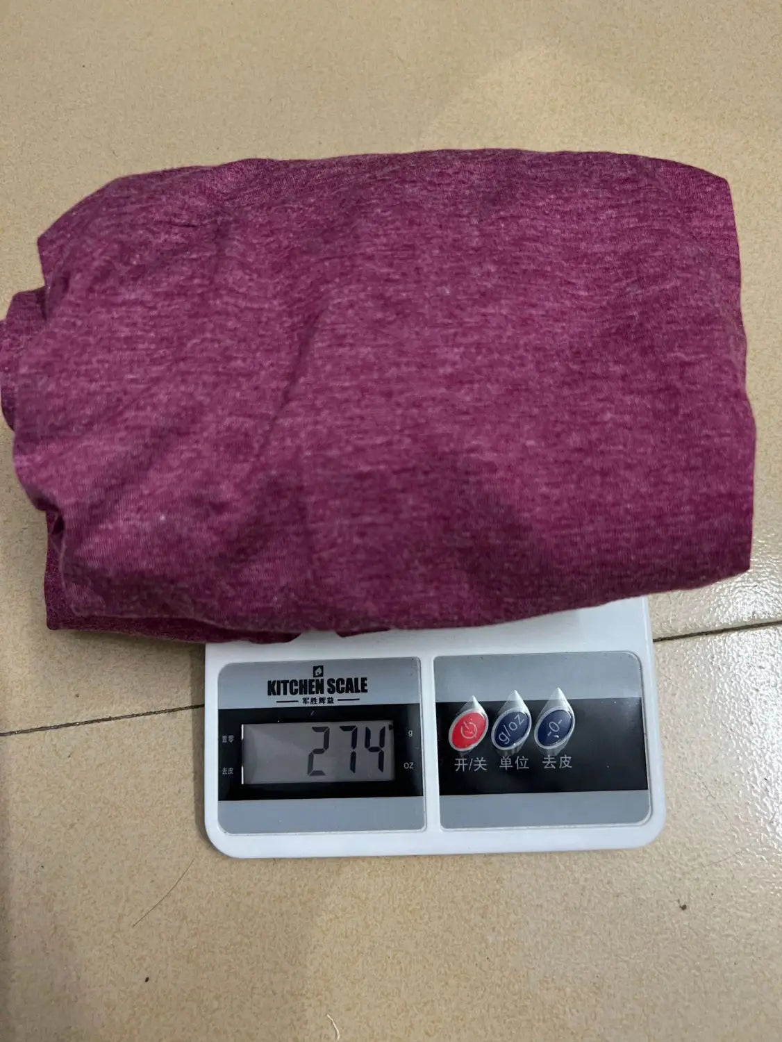 A folded maroon heathered Twist Front v Neck short sleeve midi dress garment resting on a digital kitchen scale.