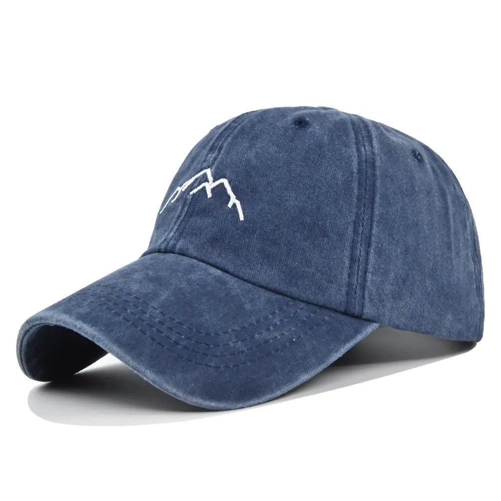 A faded navy blue denim baseball cap with a simple white embroidered mountain range design on the front titled embroidered mountain baseball cap.