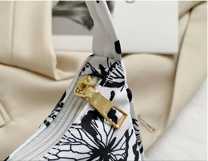 Animal print underarm shoulder bag for women featuring a black and white floral-patterned fabric with a gold-toned zipper pull.