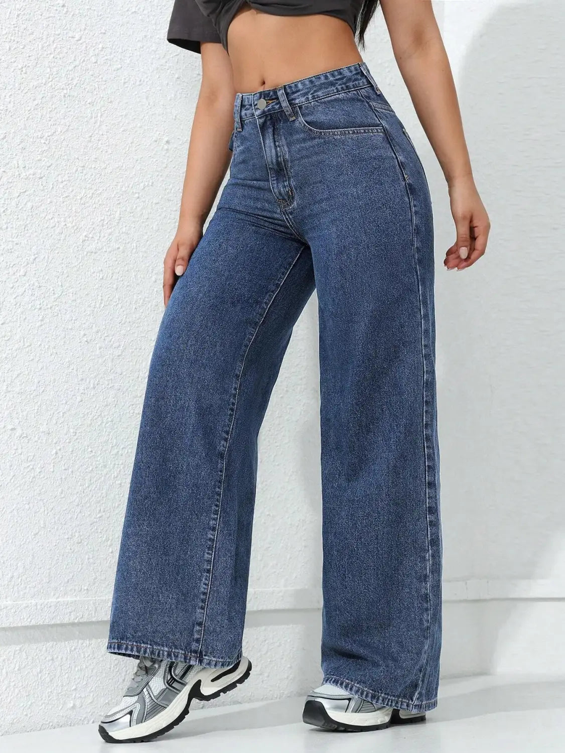 Jean en denim à taille haute, jambe large et évasée, en lavage bleu moyen, avec une couture classique et des passants de ceinture.