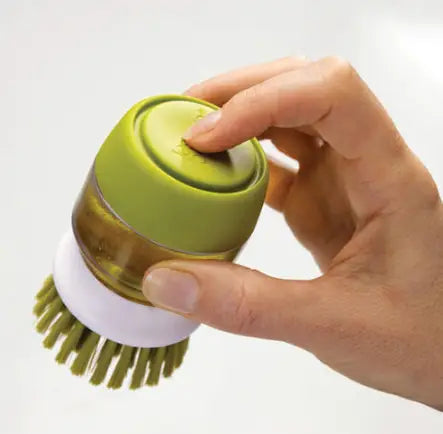 Soap dispensing dish brush with a green and white silicone scrubber and brush head featuring a non slip storage base for cleaning.