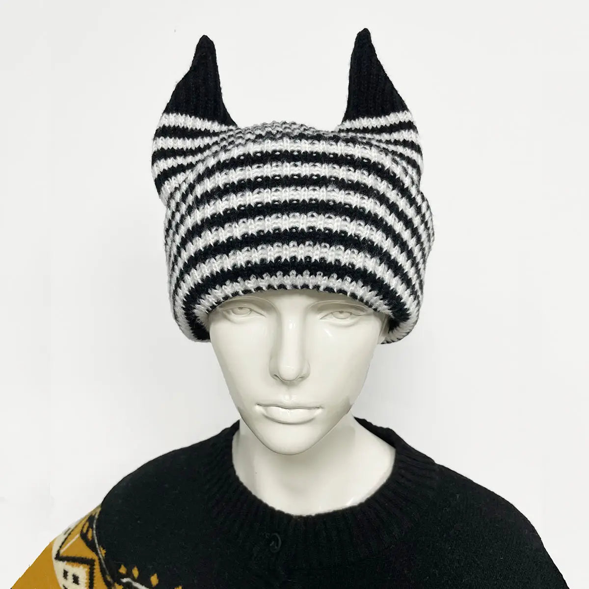 Bonnet hivernal de type cagoule tricoté à rayures noir et blanc avec des protubérances pointues en forme d’oreilles, fabriqué en laine souple.