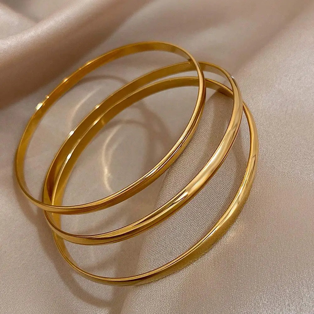 Three sleek polished gold 18k gold plated minimalist stackable bangles with a smooth reflective finish.