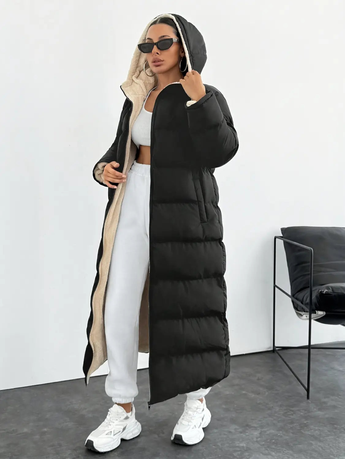 Black hooded quilted long puffer coat in black with a beige-lined hood and front zipper featuring quilted panels.
