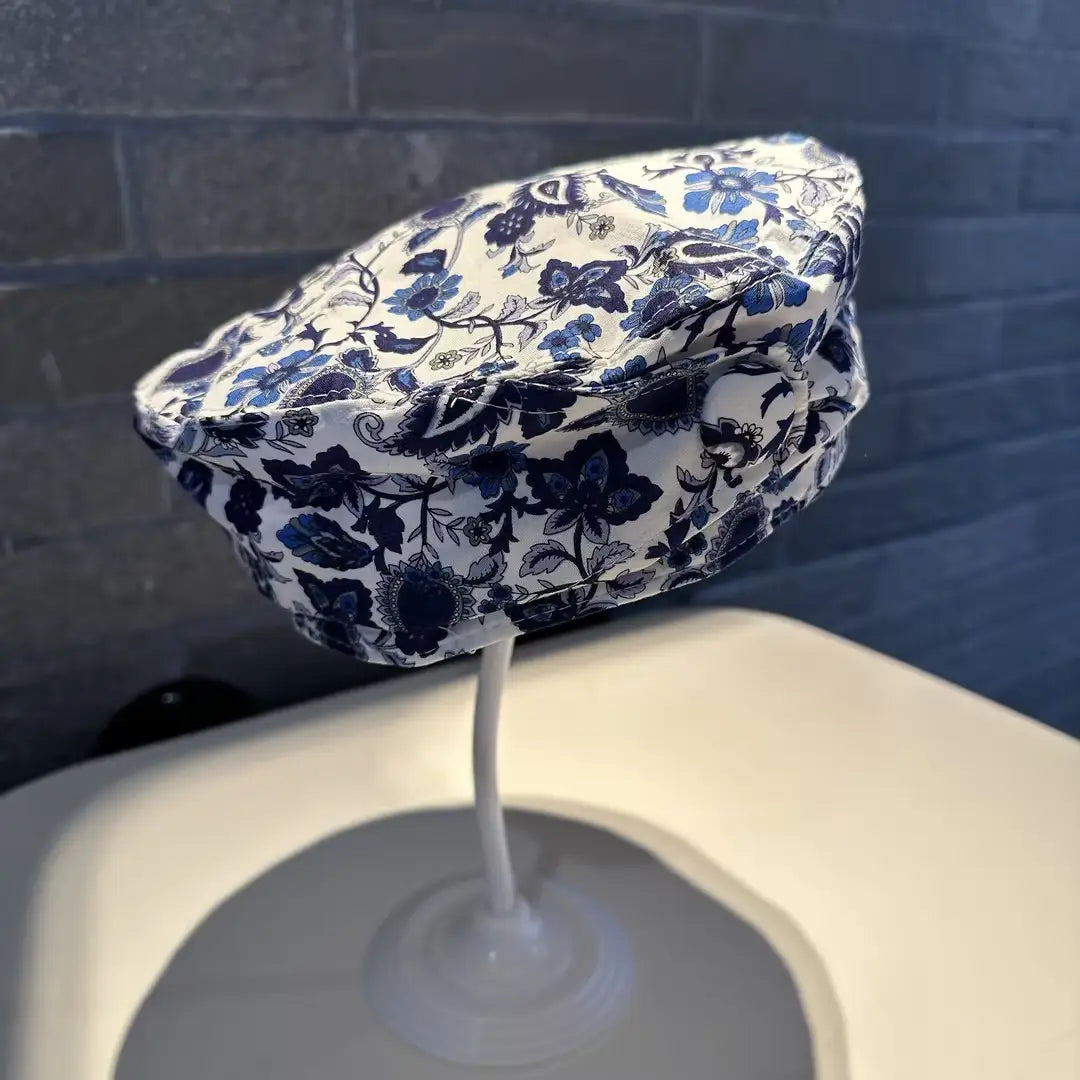 A white fabric printed Korean style fashion cap with a blue floral pattern and intricate botanical designs featuring a soft slightly wrinkled texture.