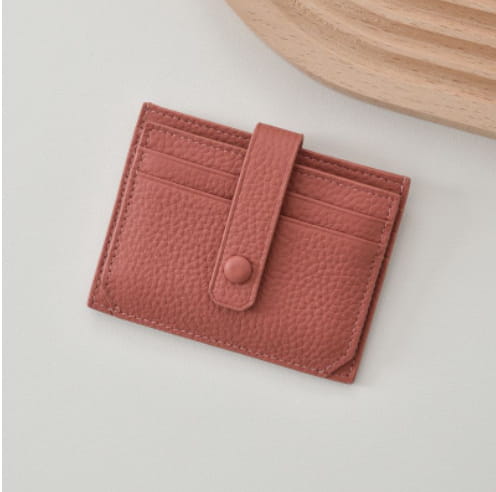 Ultra thin minimalist rose-colored leather card holder with textured surface and single button closure.