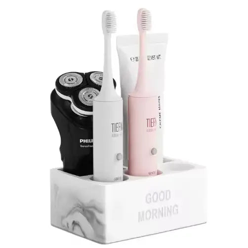 White marble-textured ceramic toothpaste holder rectangular bathroom organizer holding a black Philips electric shaver and white and pink tier toothbrushes with matching tubes.