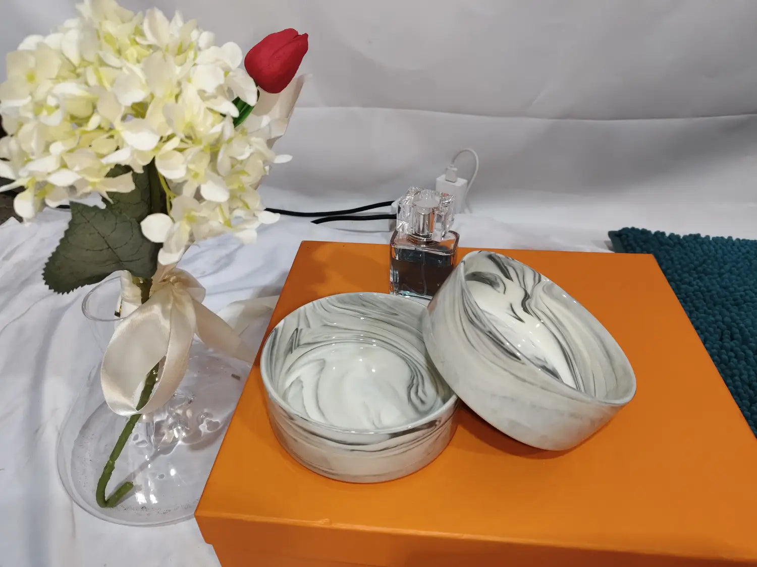 White and gray marble-patterned ceramic double pet bowl with matching lid resting on an orange box with a wood stand.