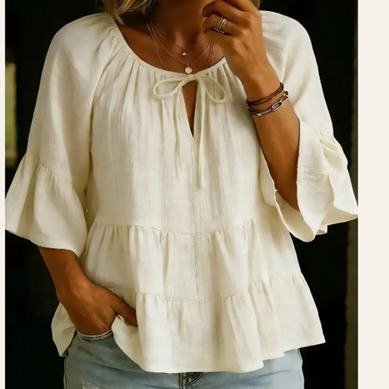 Blusa de algodón y lino plisada color blanco roto, suave, con escote fruncido atado con un lazo y mangas campana acampanadas.