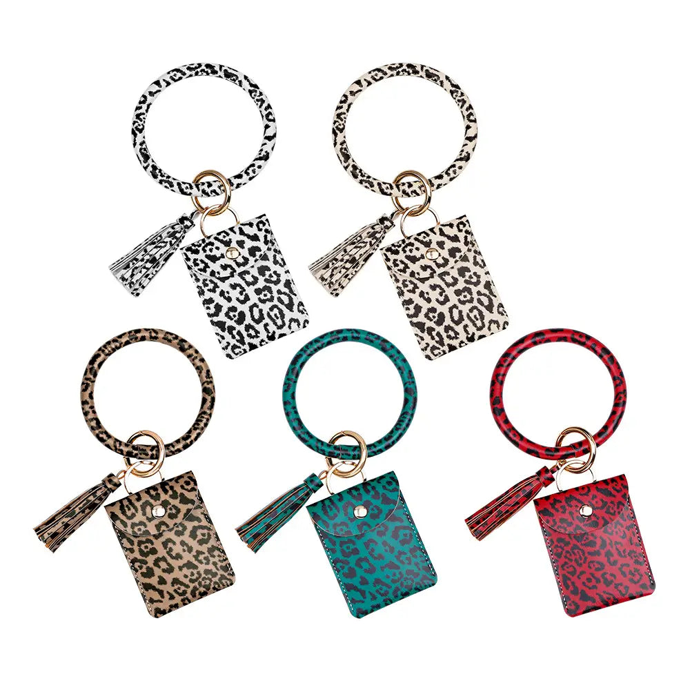 Porte-cartes avec mousqueton de poignet en cuir, avec glands, dans des tons imprimé léopard noir, brun, bleu-vert et rouge, en cuir.