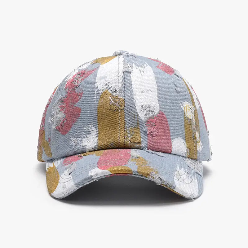 Une casquette de baseball en coton à projections de peinture vieillies, en denim, présentant un motif abstrait délavé de touches rose, blanc et jaune moutarde.