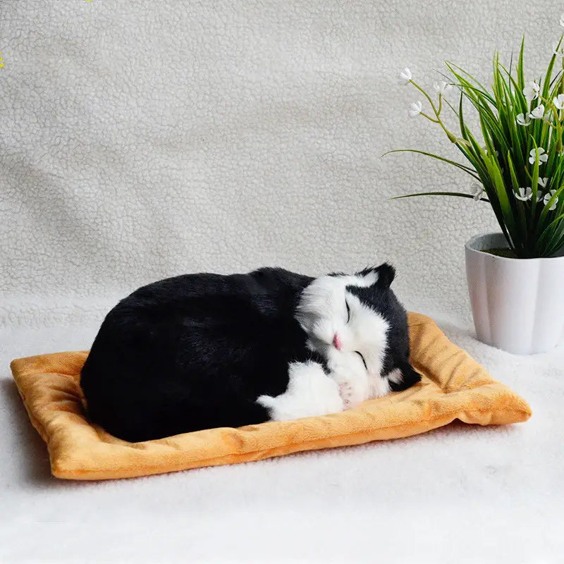 realistic breathing plush cat figurine in black and white resting on a soft orange cushion pet bed