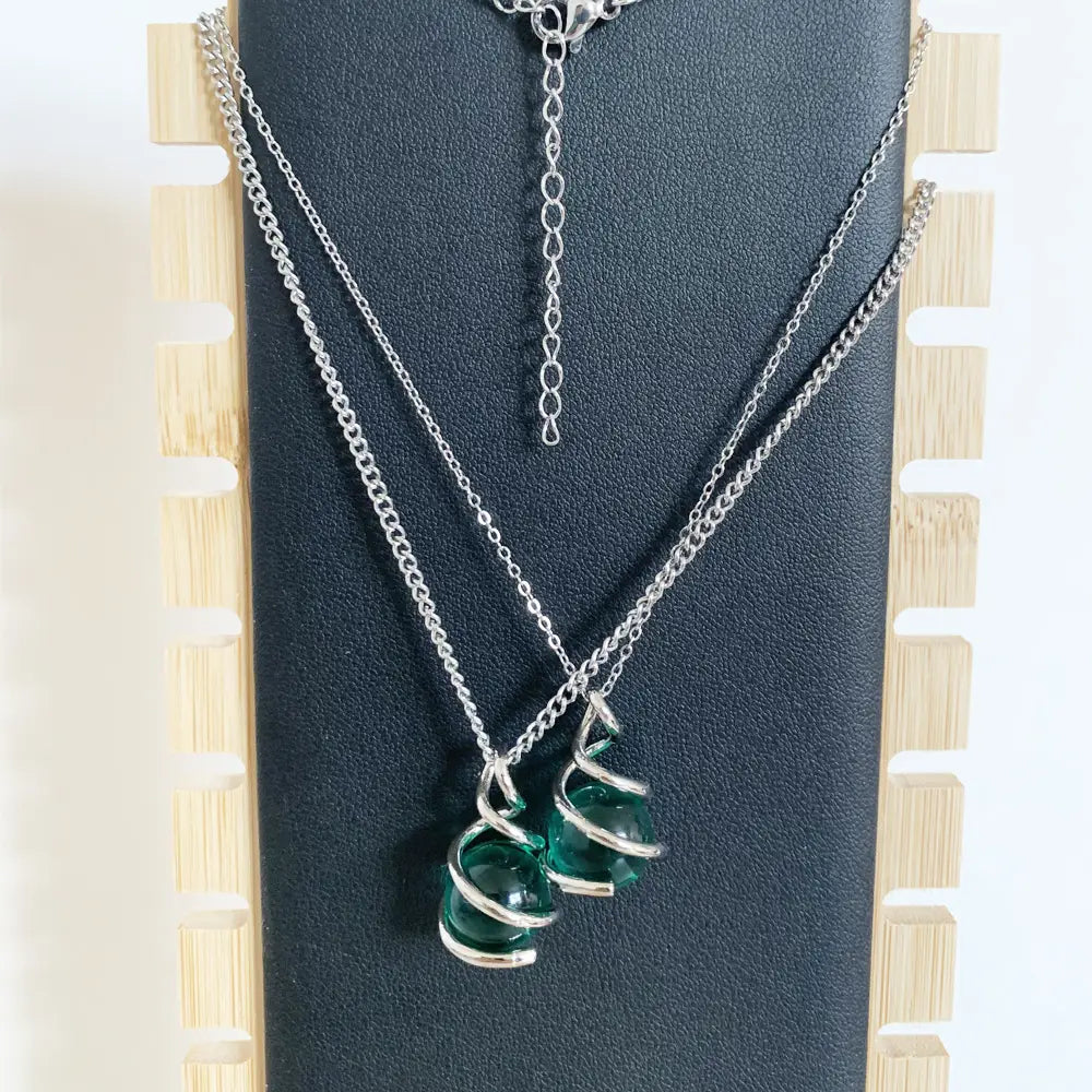Collar de cadena de plata que presenta un colgante esférico de vidrio color verde esmeralda con dos cuentas, envuelto en un diseño en espiral de alambre de plata retorcido.