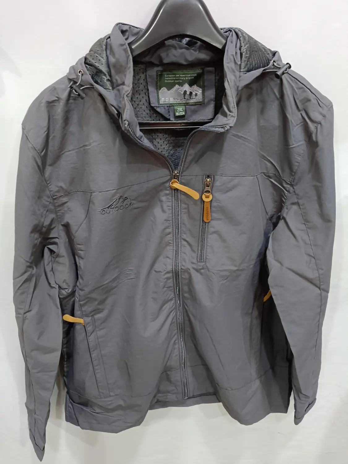 Chaqueta de senderismo con capucha impermeable color gris, con tiradores de cremallera color camel y una marca sutil en el pecho, diseñada para actividades al aire libre.