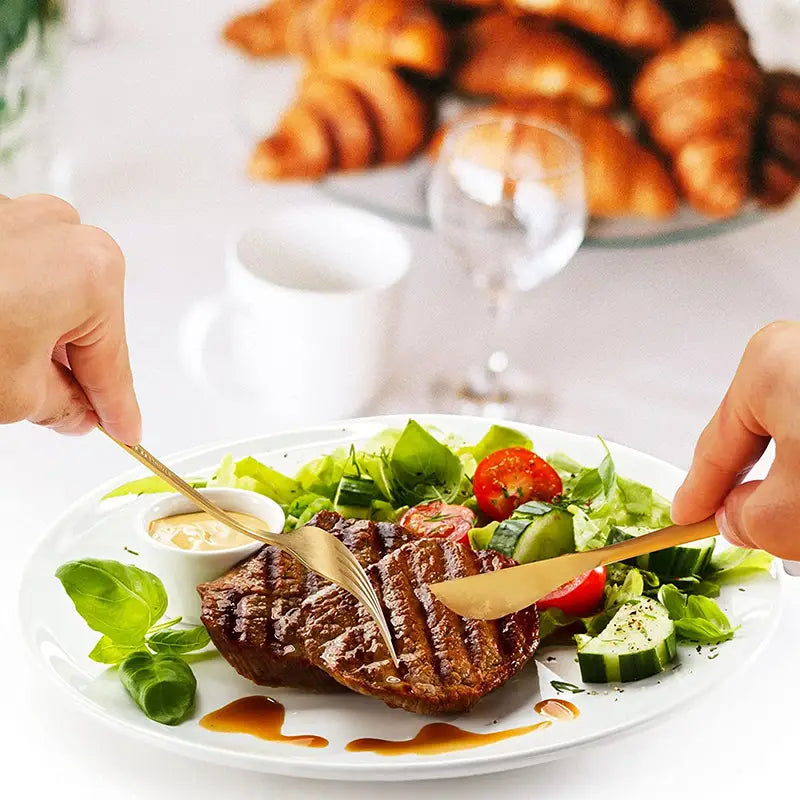 golden stainless steel matte cutlery set resting on a white plate with grilled steak and fresh salad showcasing minimalist flatware.