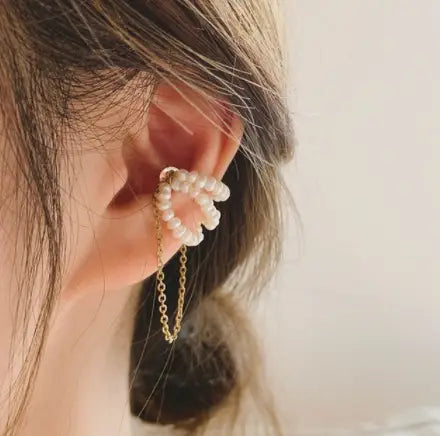 A delicate gold-toned butterfly and diamond alloy ear cuff adorned with a cluster of small white pearls and featuring a dangling chain.