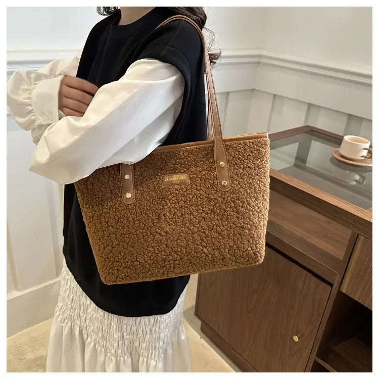 A cozy tan brown faux fur tote bag with brown leather handles and a matching brand plaque.