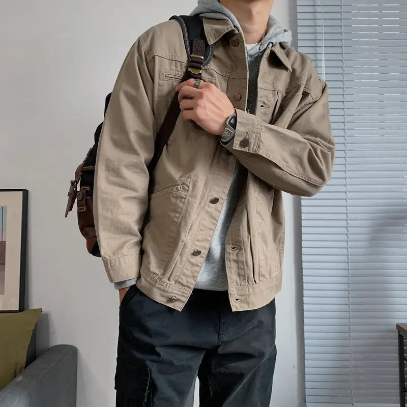 Beige utility jacket with button closures and flap pockets paired with mens black denim jacket casual retro utility outerwear.