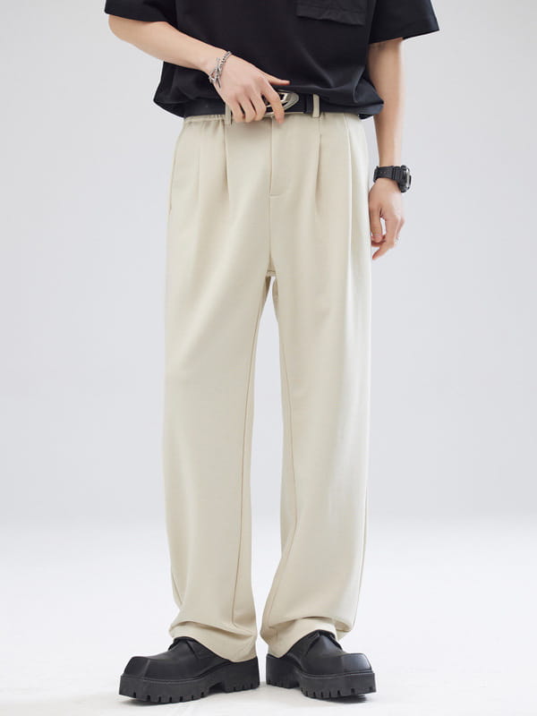 Pantalon pour hommes beige à plis et coupe ample à jambes larges et ajustement décontracté, avec une surpiqûre verticale discrète.