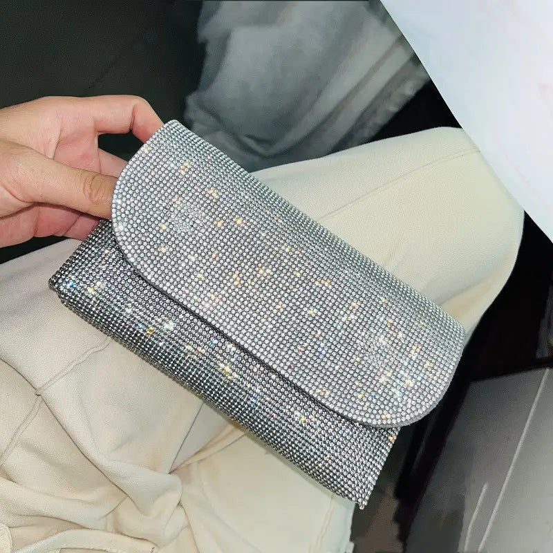 きらめくラインストーンを密にあしらった、輝きのあるシルバー表面を特徴とする、シルバーのチェーンストラップ付きラインストーン・クラッチバッグ。