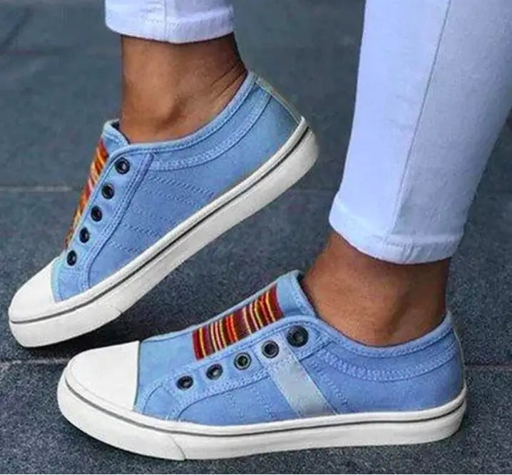 Helleblaue schnürlose Canvas-Sneaker mit weißen Gummisohlen, schwarzen Ösen und einem farbigen gestreiften Akzent sowie seitlich aufschlüpfbare Loafer.