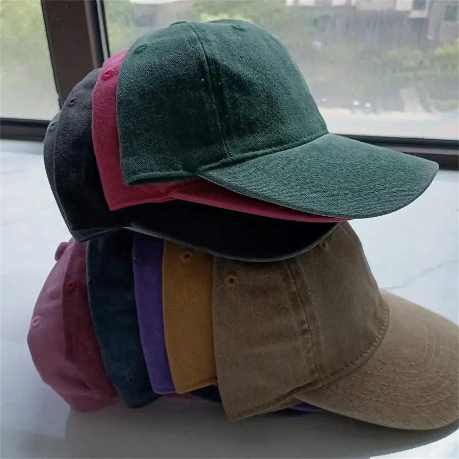 Stack of colorful cotton baseball caps in muted tones including forest green dusty rose black and tan featuring a vintage washed sun hat design.