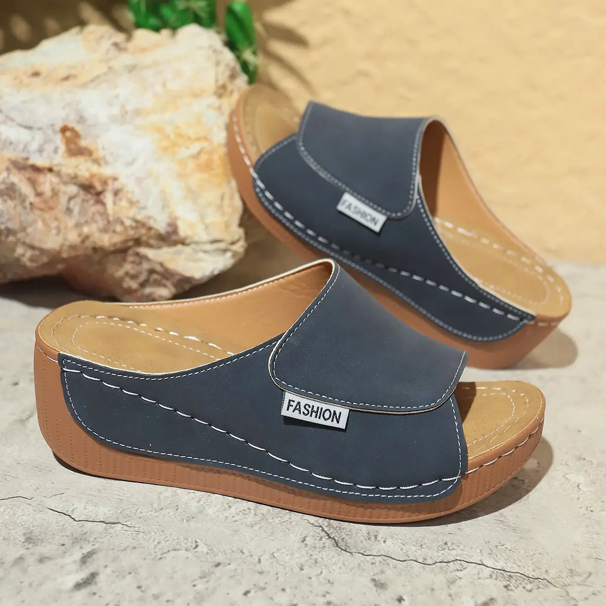 Sandales d’été à plateforme compensée à bride glissante pour femmes en daim gris foncé, avec une semelle en caoutchouc beige, des coutures blanches et une petite étiquette de mode sur la bride.