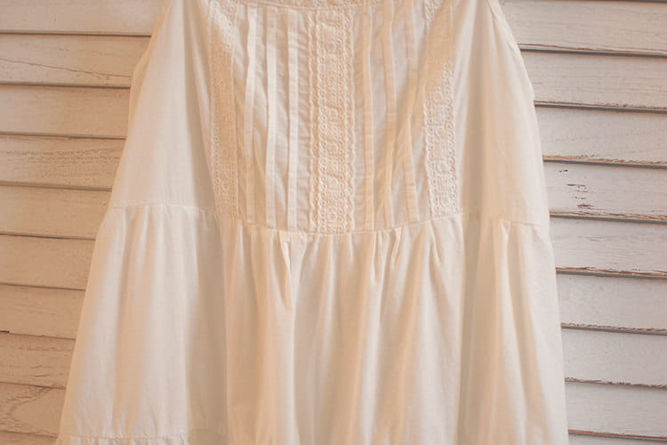 Ein zartes cremefarbenes Baumwoll-Spitzenkleid mit Volants (gestufter Rock) mit aufwendiger Spitzenstickerei am Oberteil und sanften gerafften Details.