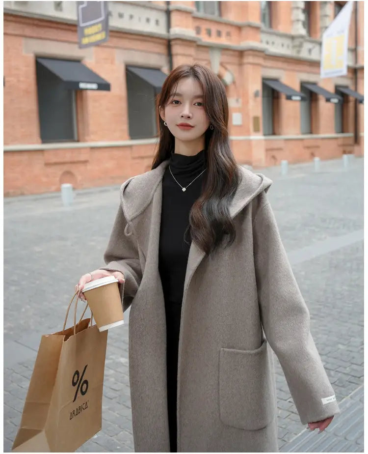 Beiger Wollmantel als Winter-Outdoorbekleidung mittlerer Länge mit Kapuze und vorderer Tasche, gefertigt aus Wolle.