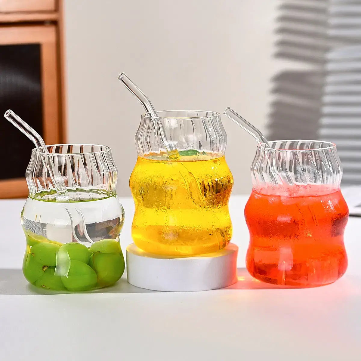 Drei klare gerippte Glasbecher mit geschwungenen Strohhalmen, gefüllt mit Getränken in unterschiedlichen Farben, und unterschiedlich garniert aus dem gerippten Glasbecher-Set mit Strohhalmen, 6-teiliges Set, 19 oz.
