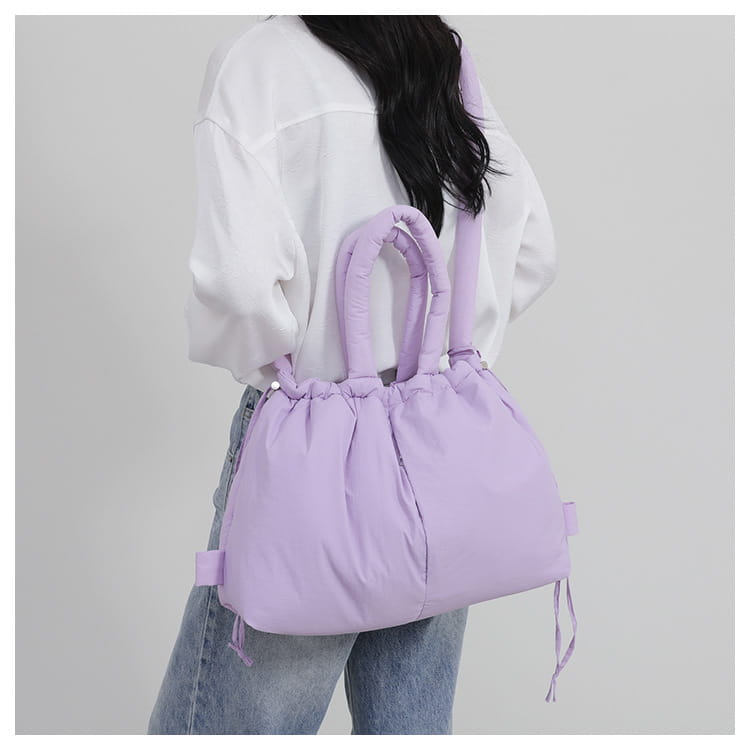 A soft lavender quilted puffer tote bag made of lightweight nylon with padded handles and drawstring ties for shoulder use.