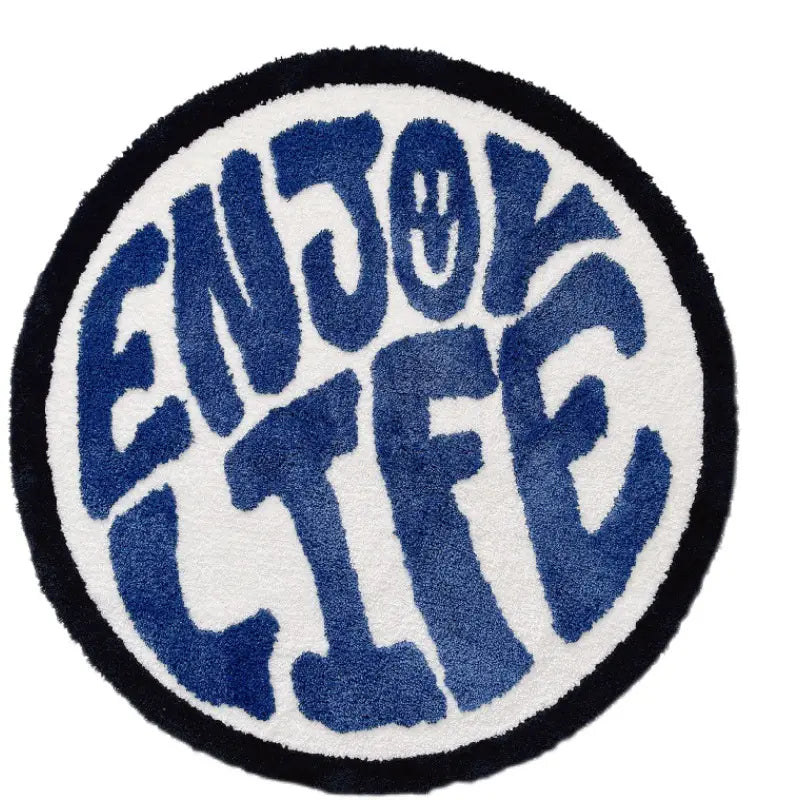 A circular plush rug with a minimalist enjoy life print in bold blue lettering on a white background framed by a black border.