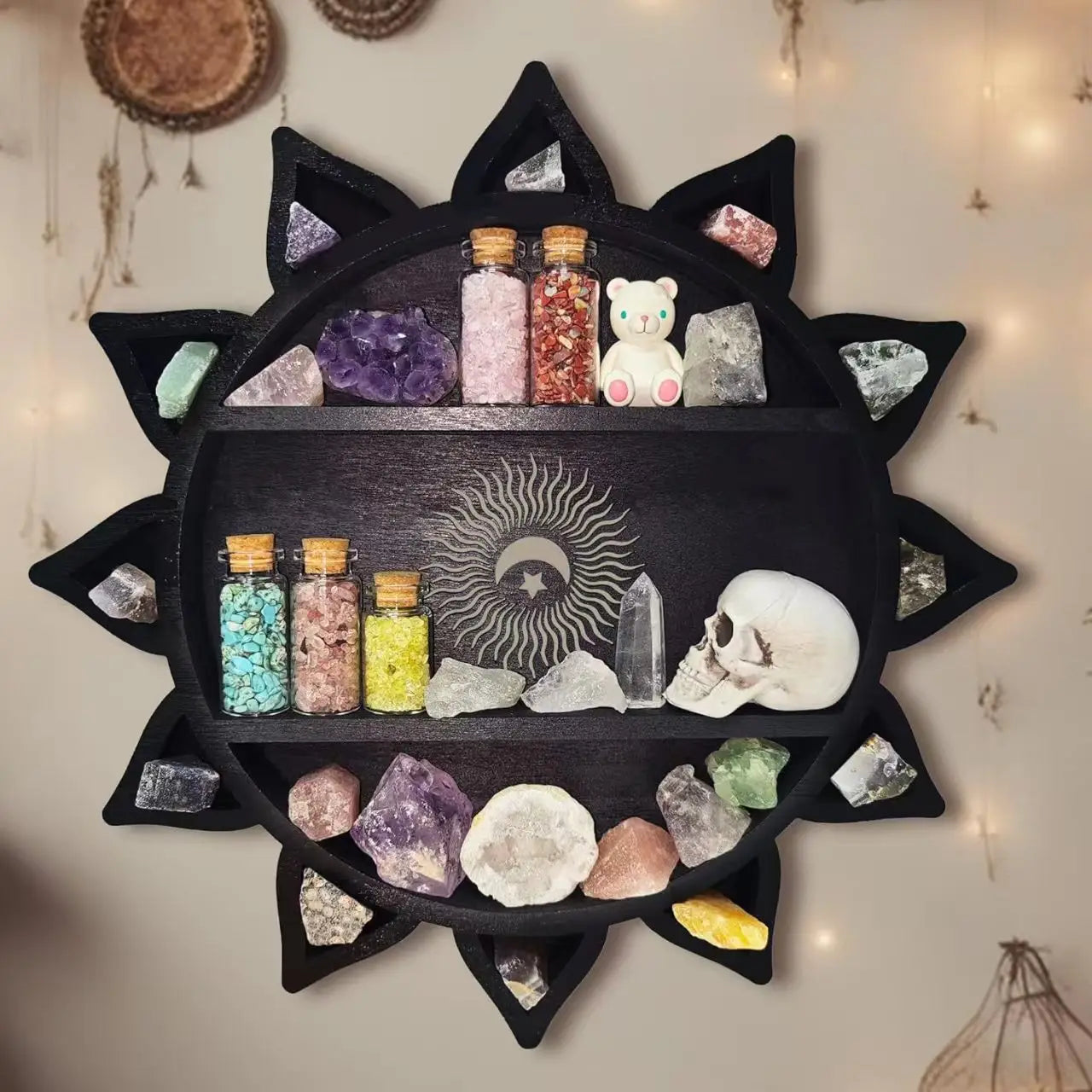 Black sun-shaped wooden floating shelf with three tiers displaying crystals bottles and a small white teddy bear for crystal display and storage.