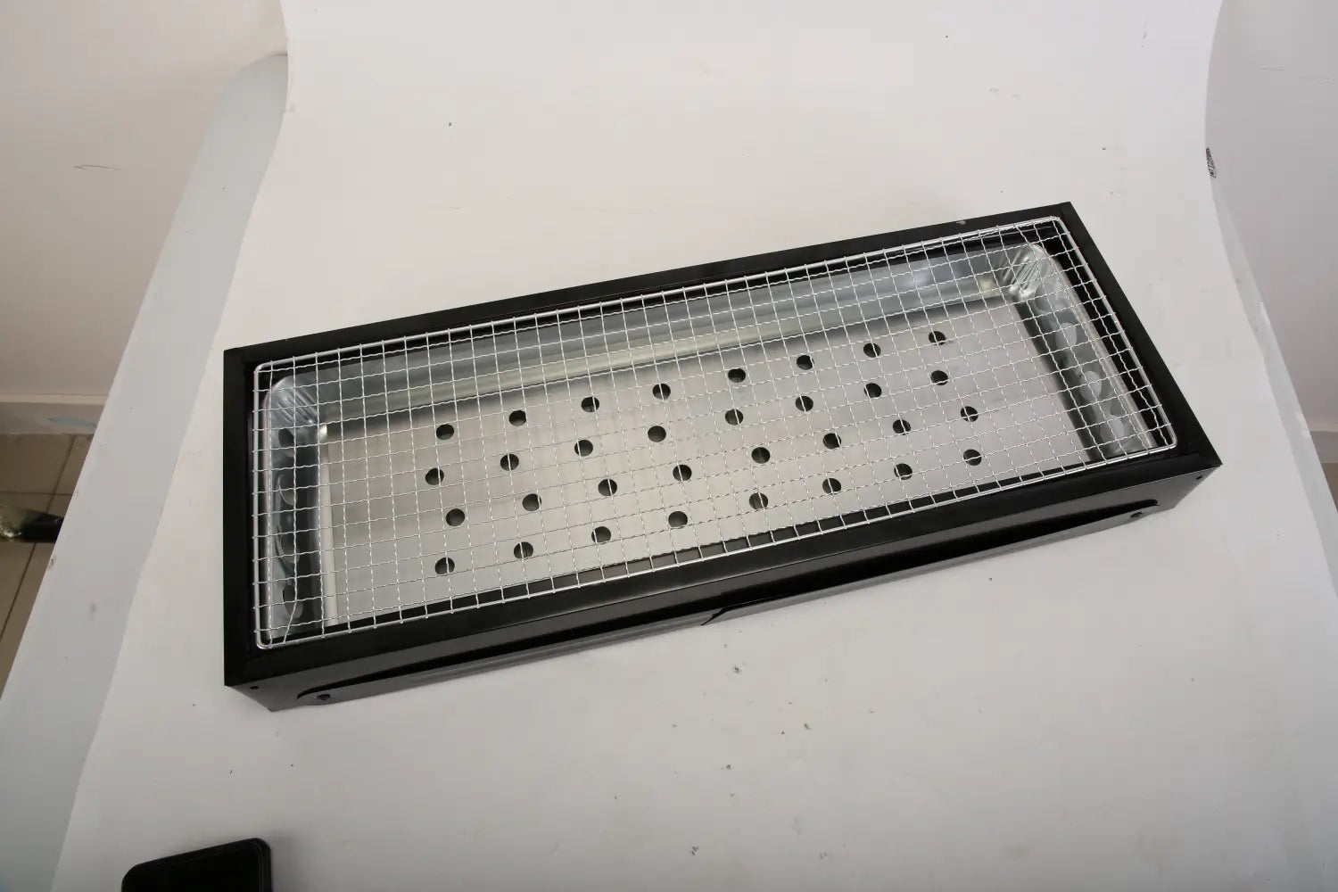 Black portable charcoal BBQ grill featuring a foldable stainless steel mesh grate with evenly spaced circular holes.