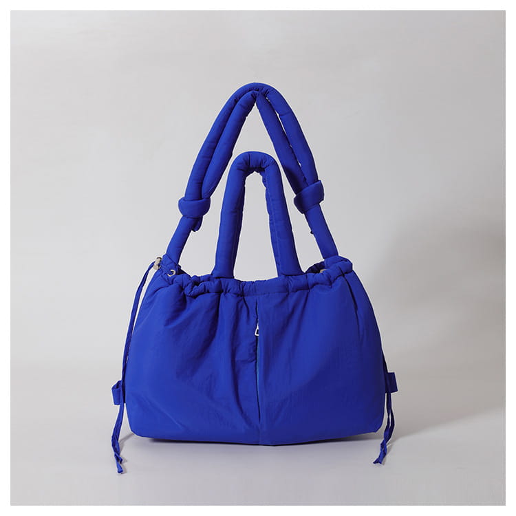 Vibrant royal blue quilted puffer tote bag made of lightweight nylon with thick quilted handles and a drawstring closure for convenient shoulder use.