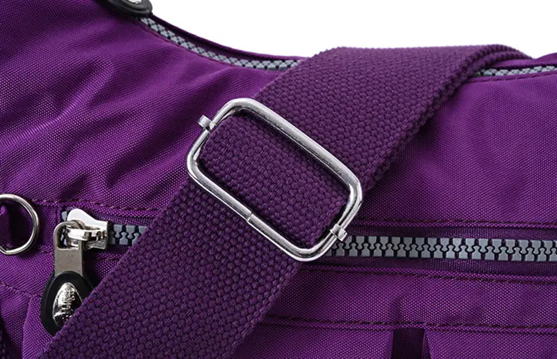 Purple nylon shoulder strap with silver-toned metal buckle and zipper details on a waterproof multi pocket nylon crossbody shoulder bag.