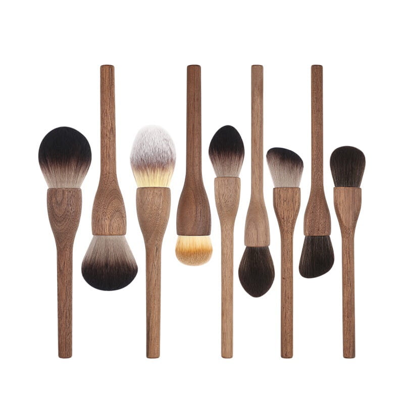 Set of eight walnut wood makeup brushes with wooden handles and soft natural fiber bristles in varying shapes and shades.