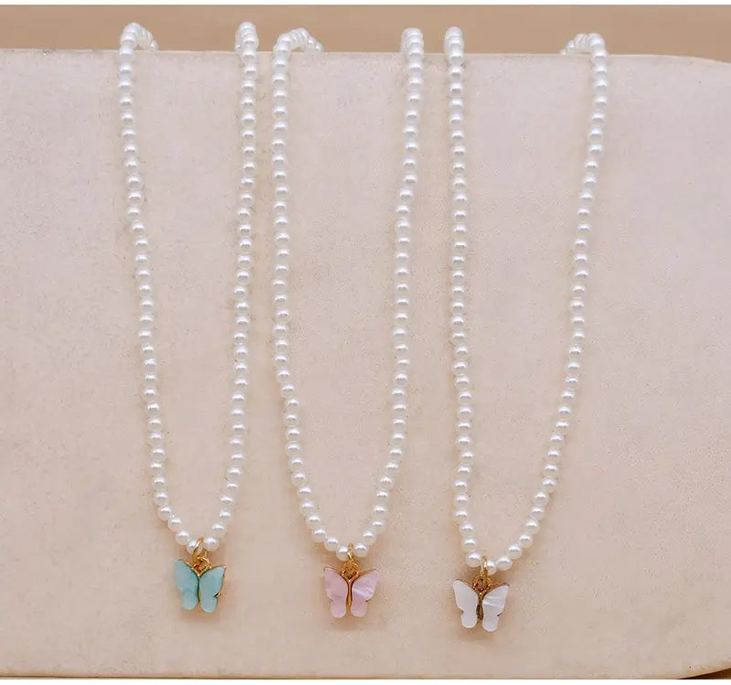 Three delicate pearl choker necklaces each featuring a small butterfly pendant in pastel blue pink and white in the elegant pearl butterfly charm choker necklace collection.
