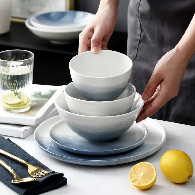 Set of three nested ceramic steak plates and bowls with a smooth gradient finish transitioning from white to soft blue.