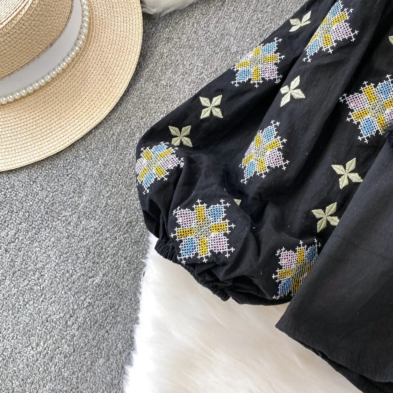 Black embroidered lantern sleeve tie neck blouse with colorful blue yellow and green cross-stitch patterns on soft fabric