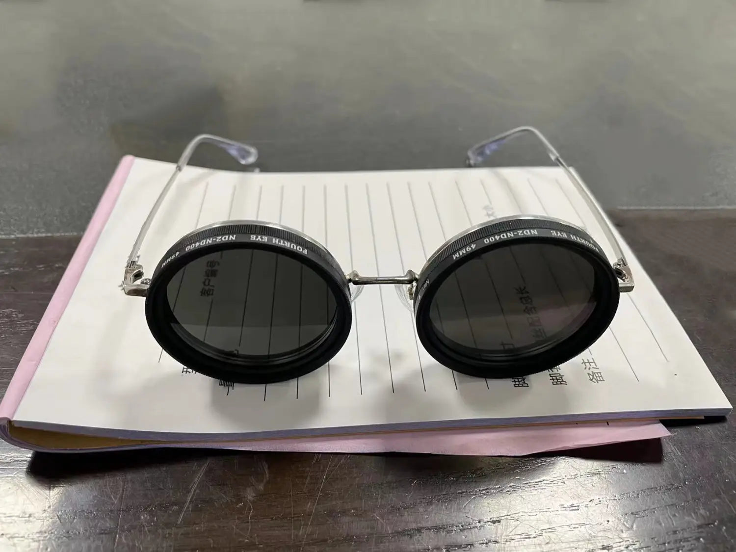 Lunettes de soleil rondes unisexes résistantes aux UV, à monture argent métallique et verres circulaires noirs, posées sur un carnet à lignes.