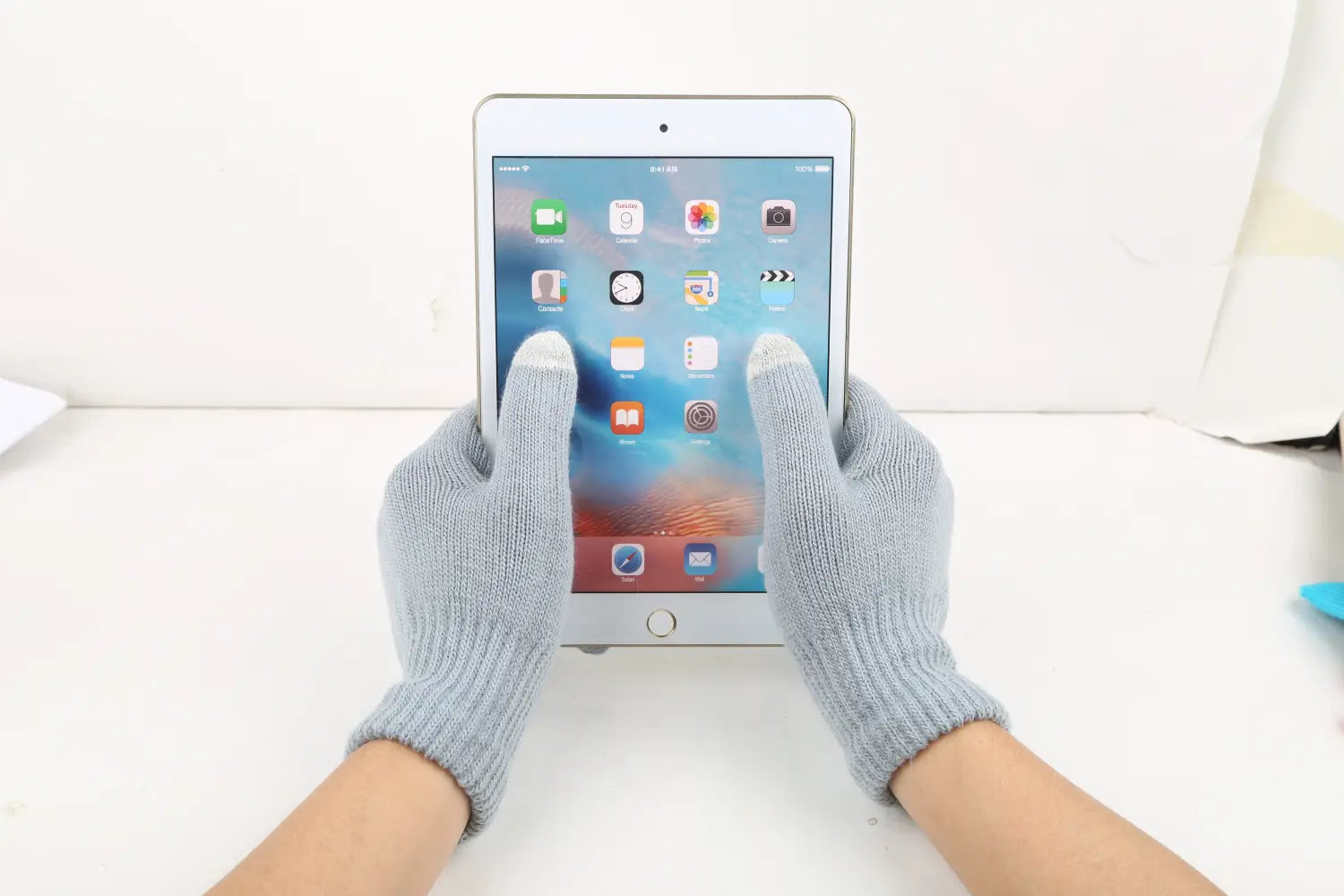 Hände, die hellgraue, gestrickte Touchscreen-Winterstrickhandschuhe tragen, halten ein weißes iPad mini mit silbernem Rahmen und Home-Button und demonstrieren Wärme und Benutzerfreundlichkeit.