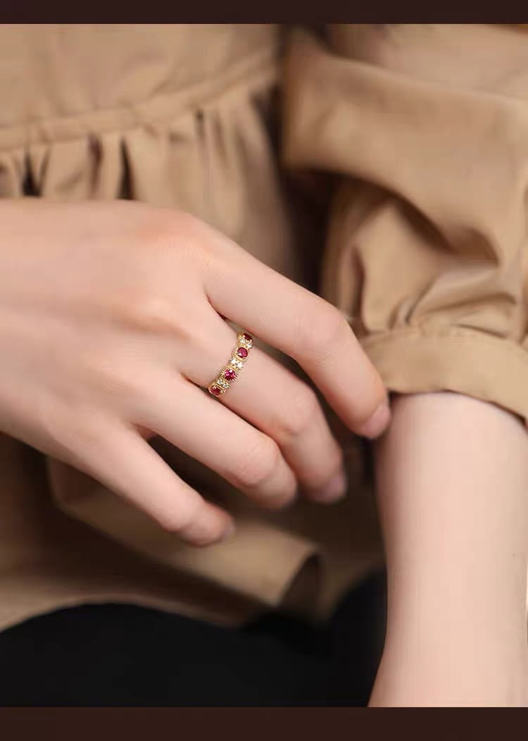 An 18k gold plated band ring adorned with evenly spaced pigeon blood ruby gemstones and diamond accents.