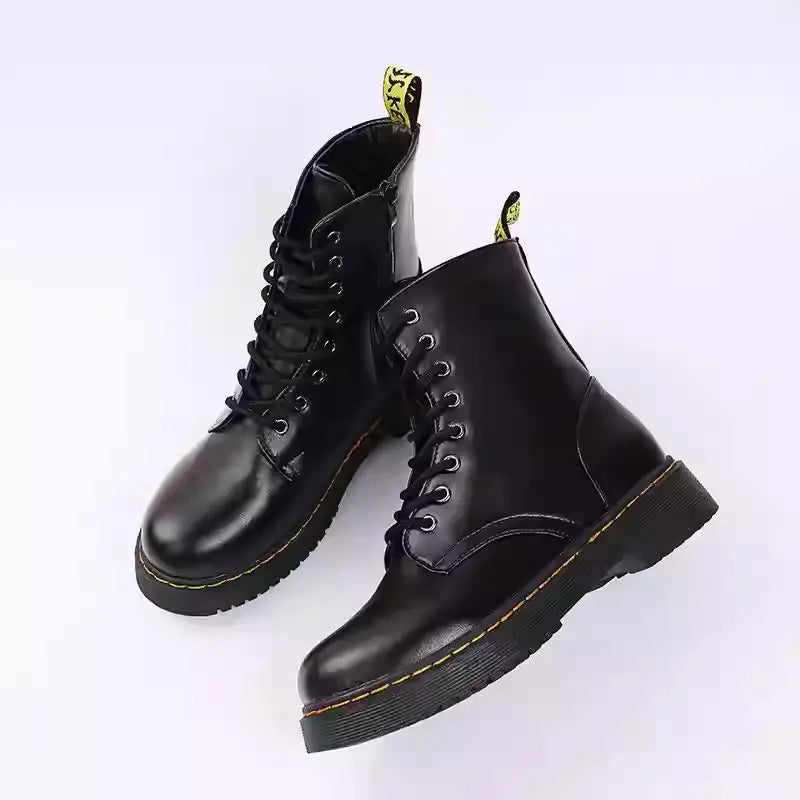 Botines estilo Martin de cuero negro con punta redonda, diseño plano a la altura del tobillo, costuras amarillas, cierre con cordones y lengüetas de extracción.