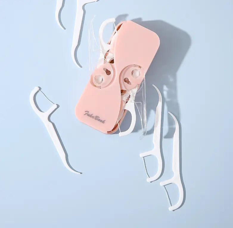 boîte de rangement pour fil dentaire en plastique rose avec étui à ouverture automatique, entourée de cure-dents blancs pour fil dentaire